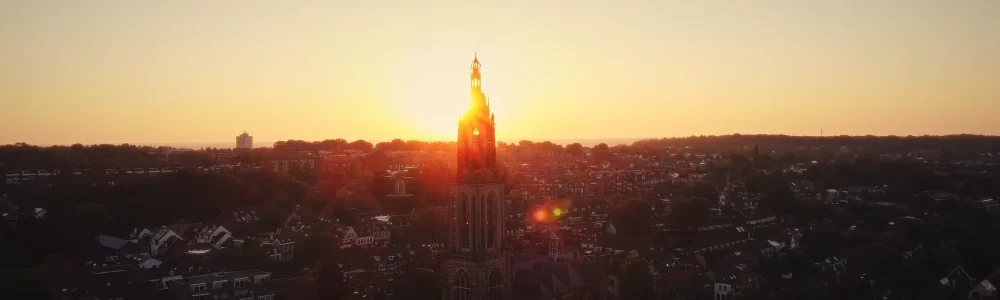 Dronefoto van de Cunerakerk in Rhenen bij zonsopgang, vastgelegd in warm ochtendlicht.